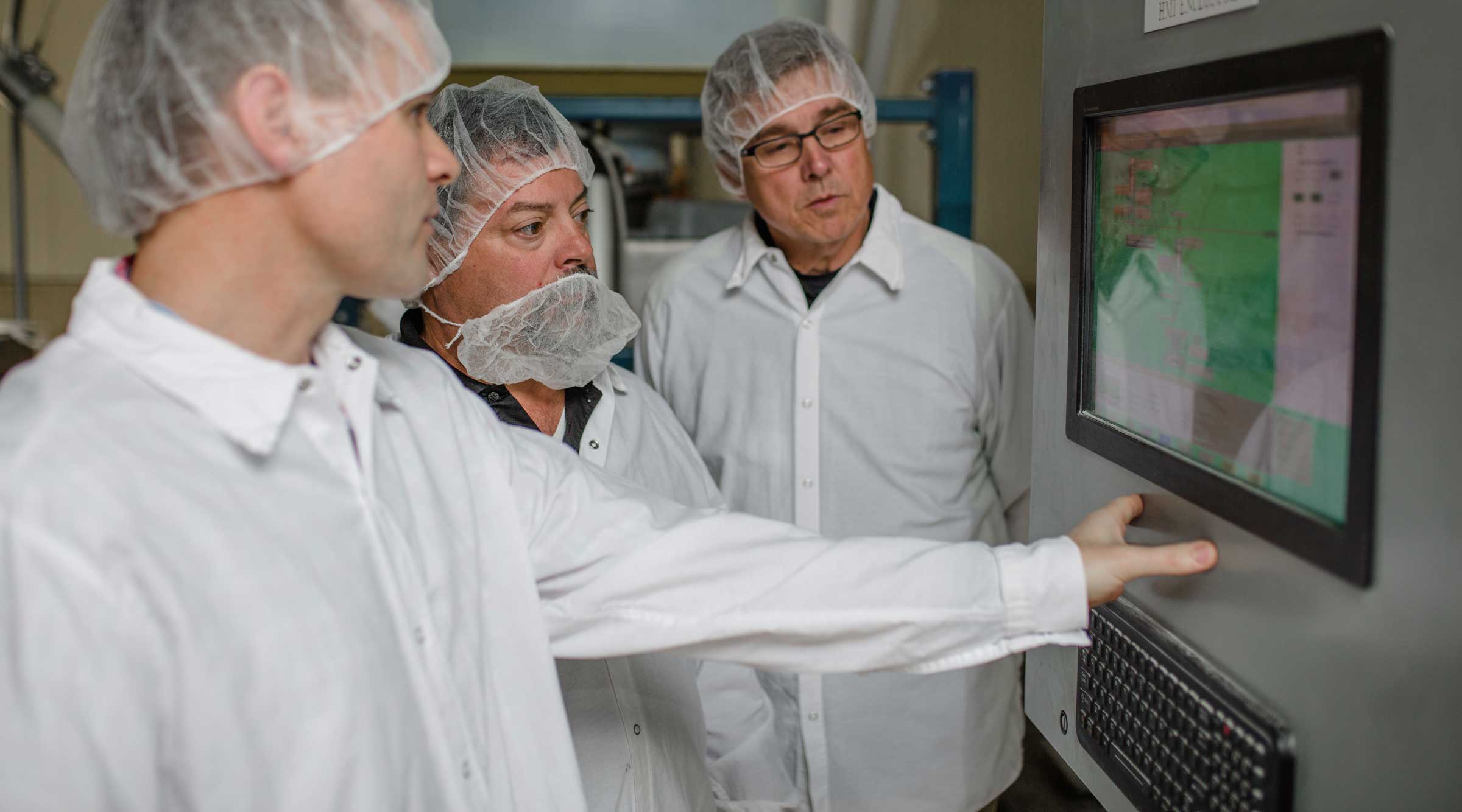 Three men in smocks checking settings on equipment