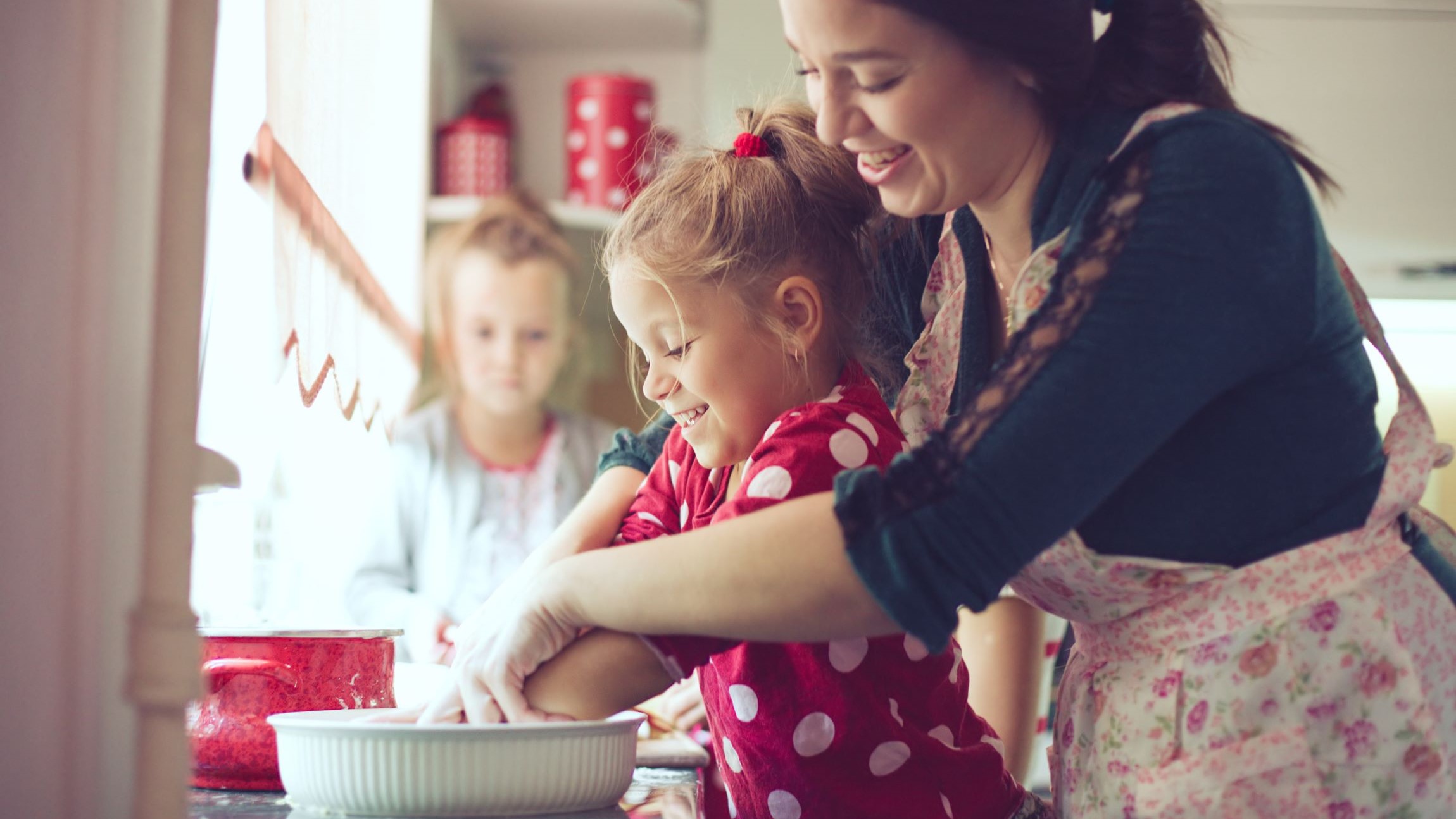 Mom and two daughters mixing something in a bowl in the kitchen